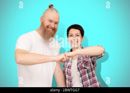 Beautiful cheerful happy couple 40s bumping fists standing on blue background. Mid adult bearded man and short cut brunette. Family unity concept Stock Photo