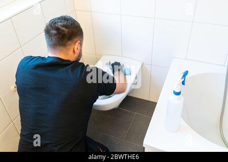 A professional cleaner cleans a ceramic toilet very thoroughly in a modern bathroom Stock Photo