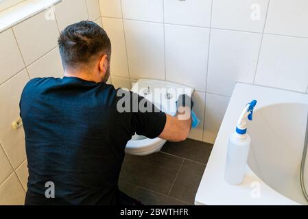 A professional cleaner cleans a ceramic toilet very thoroughly in a modern bathroom Stock Photo