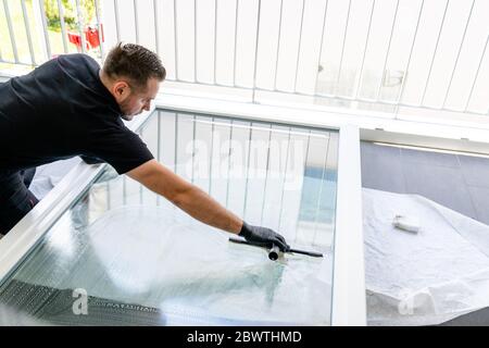 A professional window cleaner using a window cleaner squeegee to clean a large fold down apartment window Stock Photo