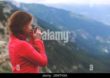 Closeup photo of cup with tea in traveler's hand over out of focus mountains view. A young tourist woman drinks a hot drink from a cup and enjoys the scenery in the mountains. Trekking concept Stock Photo