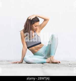 Fit sporty active girl in fashion sportswear sitting on the floor in front of gray wall. Stock Photo