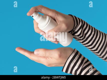 Hands using a white spray bottle, isolated against a blue background Stock Photo