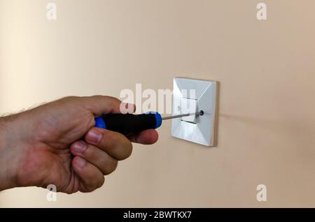 Mounting or dismounting an old light switch from a wall with a screwdriver Stock Photo