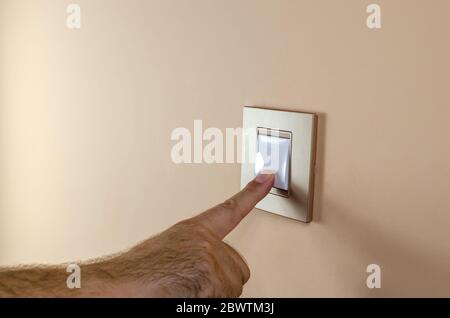 Hand pressing button of a light switch to turn light on or off Stock Photo