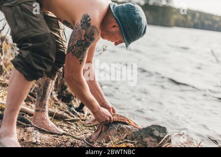 Young man gutting fish at lakeshore Stock Photo