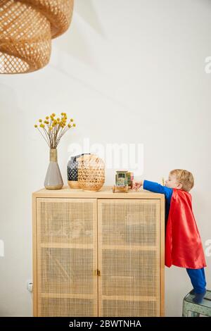 Boy wearing superman costume and reaching to wooden car on sideboard Stock Photo