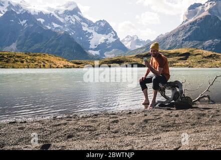 Man using cell phone in mountainscape at lakeside in Torres del Paine National Park, Patagonia, Chile Stock Photo