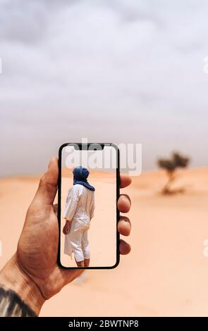 Hand holding smartphone with foto of man walking in the desert Stock Photo