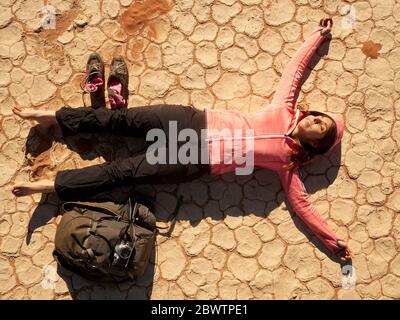 Barefoot woman and her backpack lying on the cracked dry pan floor in Deadvlei, Namibia. Stock Photo