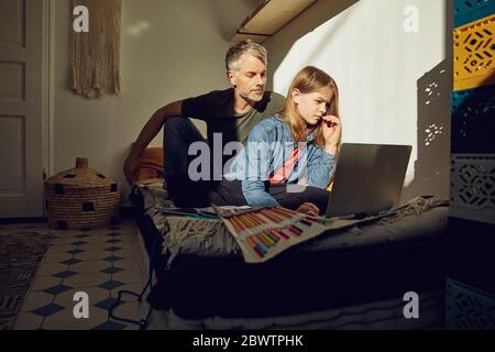 Father helping daughter doing homework and using laptop Stock Photo