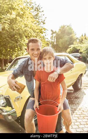 Portrait of wet boy and young man  standing in front of yellow vintage car after water fight