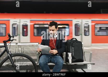Businessman with bicycle reading documents while sitting at metro station, Frankfurt, Germany Stock Photo