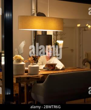 Woman working at home with digital tablet while sitting at table in living room Stock Photo