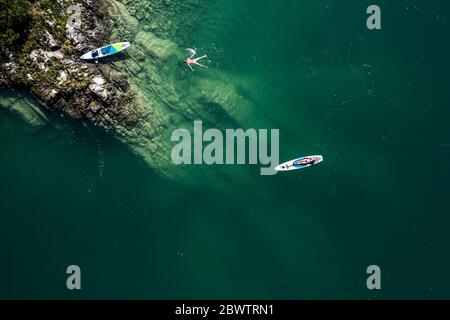 Germany, Bavaria, Aerial view of two paddleboarders relaxing on green shore of Lake Walchen Stock Photo