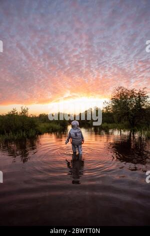 Spacewoman walking in water at sunset Stock Photo