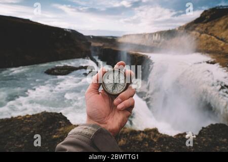 Iceland, Hand of person holding navigational compass against splashing Gullfoss waterfall Stock Photo