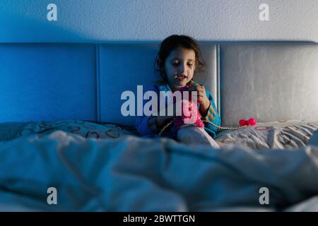 Portrait of little girl sitting on bed playing with her toy Stock Photo
