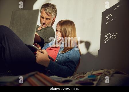 Father helping daughter doing homework and using laptop Stock Photo