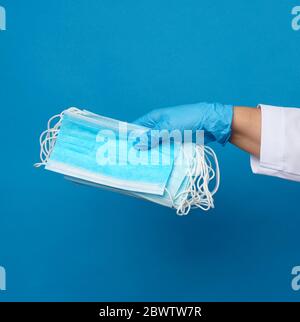 doctor in a white coat holds a stack of protective disposable face masks, blue background, protective accessory for the respiratory tract from the vir Stock Photo