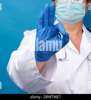 doctor in white coat shows ok gesture with his hand, concept of hope that everything will be fine, blue background Stock Photo