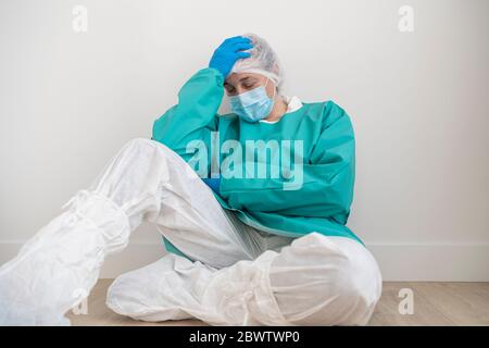 Exhausted woman wearing personal protective equipment sitting on the floor Stock Photo