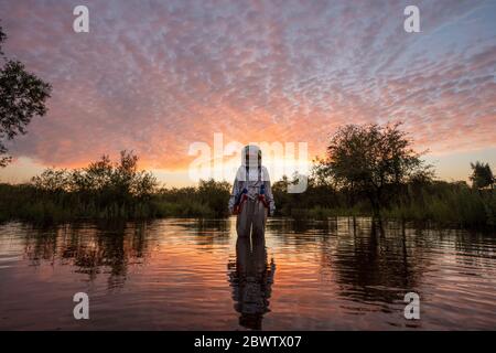Spacewoman standing in water at sunset Stock Photo