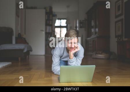 Mature woman working from home, using laptop, kneeling on floor Stock Photo