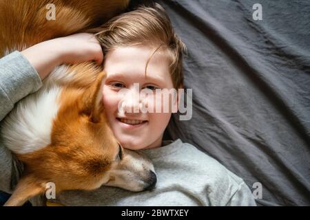 Portrait of smiling boy lying on bed cuddling his dog Stock Photo