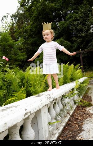 Little girl walking on a balustrade wearing cardboard crown Stock Photo