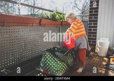 Full length of girl watering plants in balcony on sunny day Stock Photo