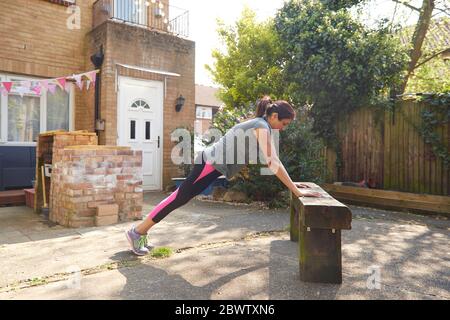 Side view of woman doing push-ups on wooden bench at back yard Stock Photo