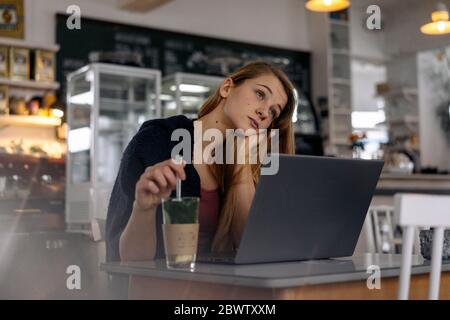 Daydreaming young woman with laptop in a cafe