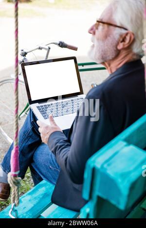 Senior man sitting outdoors using laptop Stock Photo