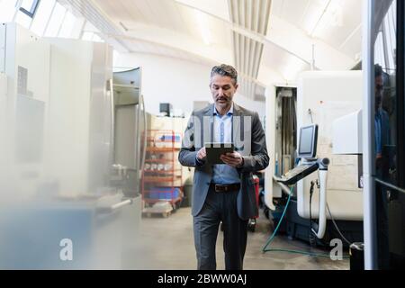 Mature businessman walking on production floor of factory, using digital tablet Stock Photo