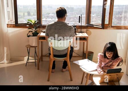 Girl doing homework while her father working on laptop in the background Stock Photo