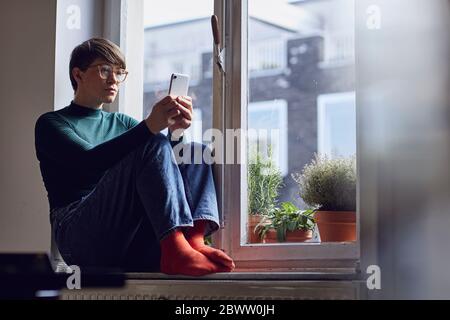 Woman sitting at the window at home using smartphone Stock Photo