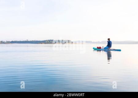 Woman sitting on sup board in the morning on a lake, Germany Stock Photo