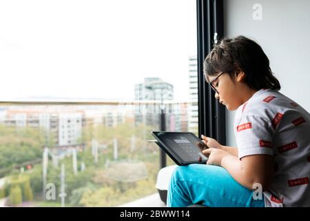 Boy sitting in front of window at home using digital tablet Stock Photo