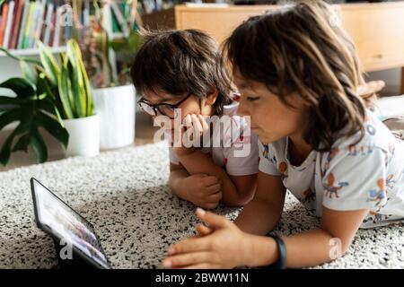Two brothers lying on the floor at home using digital tablet for video chat with their mother Stock Photo