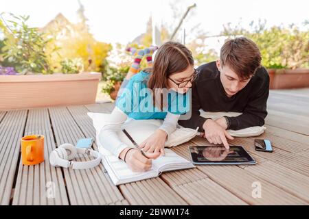 Teenage couple lying on terrace learning together with digital tablet Stock Photo