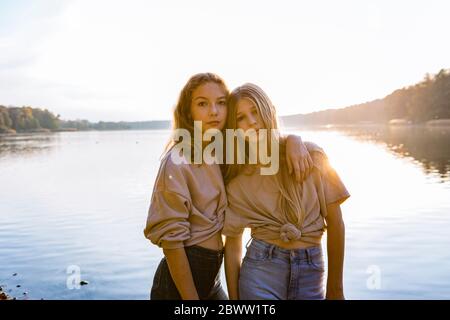 Portrait of friends standing with arm around against lake during sunset Stock Photo