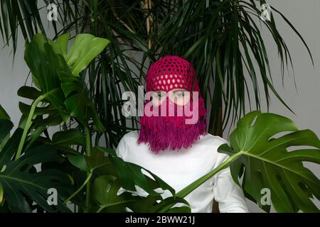 Portrait of teenage girl wearing crocheted pink headdress between house plants Stock Photo