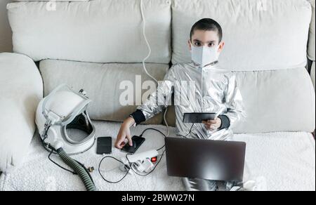 Boy playing game using laptop and smartphone, wearing space suit and protective mask Stock Photo