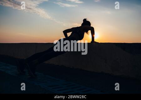 Full length of silhouette female athlete doing push-ups at promenade during sunrise Stock Photo
