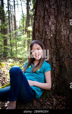 Portrait of laughing girl leaning against tree trunk in forest Stock Photo