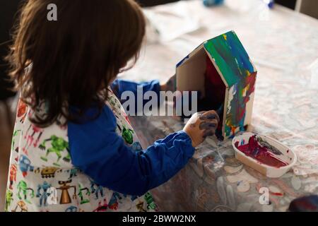 Side view of girl painting small wooden houses in living room at home Stock Photo