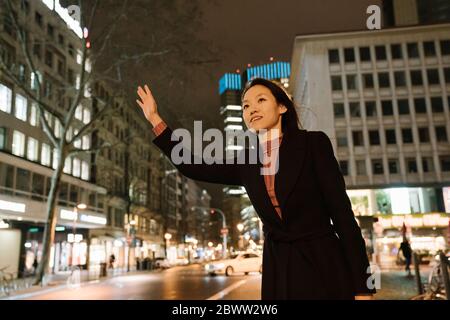 Young woman hailing a taxi in the city at night, Frankfurt, Germany Stock Photo