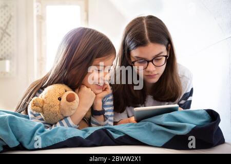 Sisters using tablet lying on bed Stock Photo