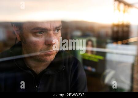Portrait of worried mature man looking out of window in the evening Stock Photo